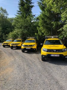 Four yellow airside operations vehicles parked on a gravel road beside some trees.