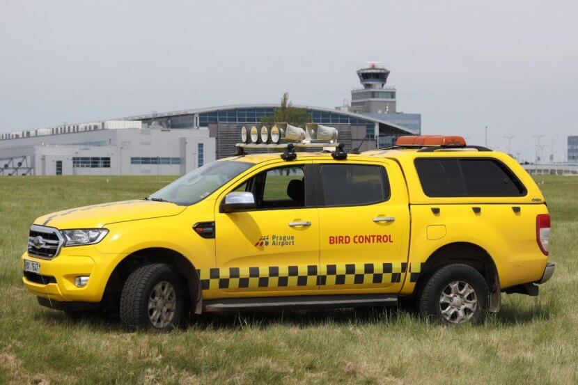 Yellow airside operations vehicle at Prague Vaclav Havel Airport on grass.