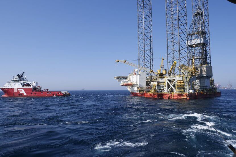 A red boat towing a small oil platform out at sea.