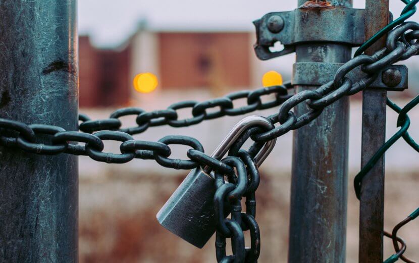 A black padlocked chain around a fence.