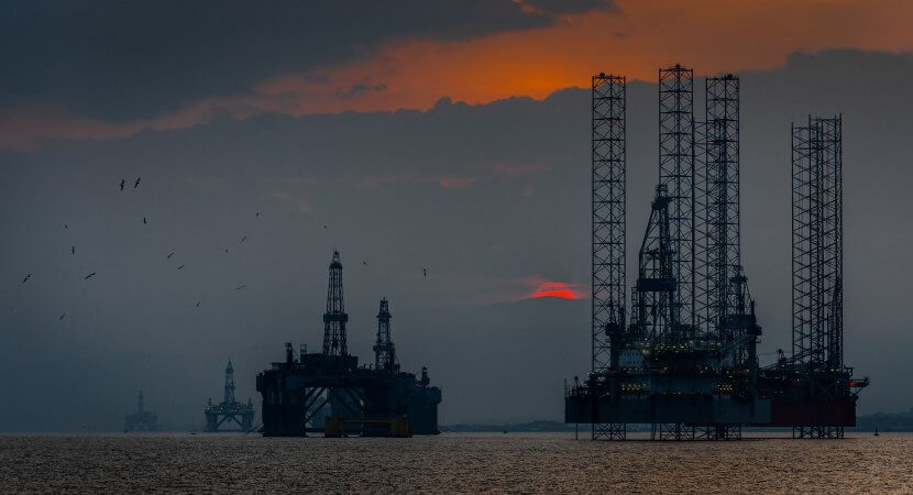 An off-shore oil platform at sunset with flocks of birds circling.