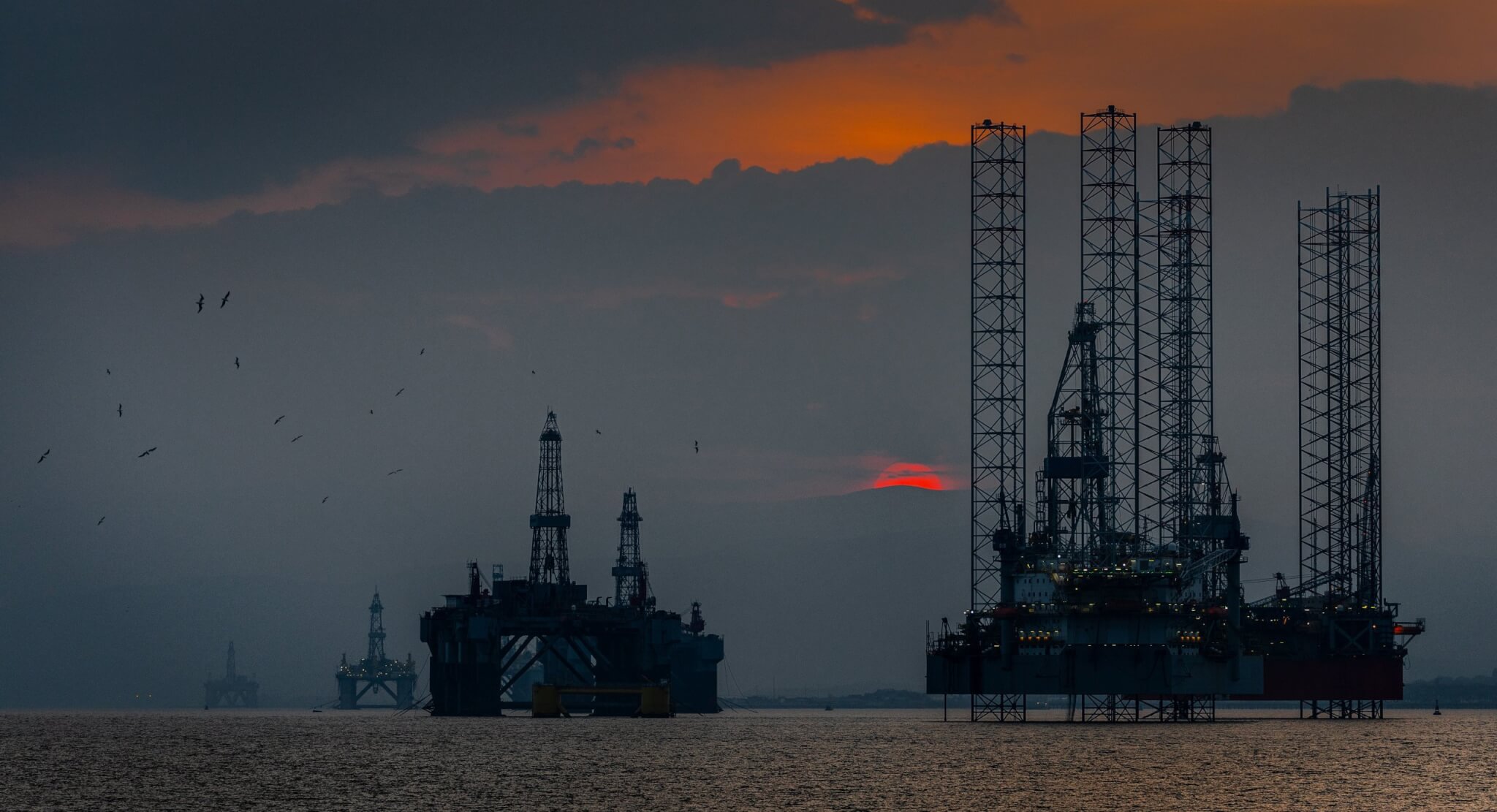An off-shore oil platform at sunset with flocks of birds circling.