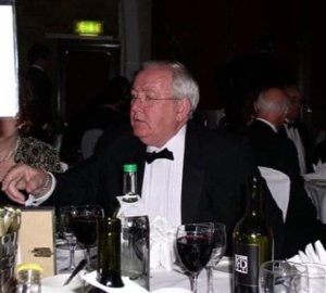 Tony Walker in a tuxedo sits at a dinner with bottles on the table.