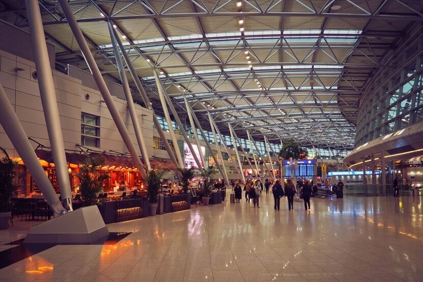 Indoor airport terminal building with a cafe and some people milling around.